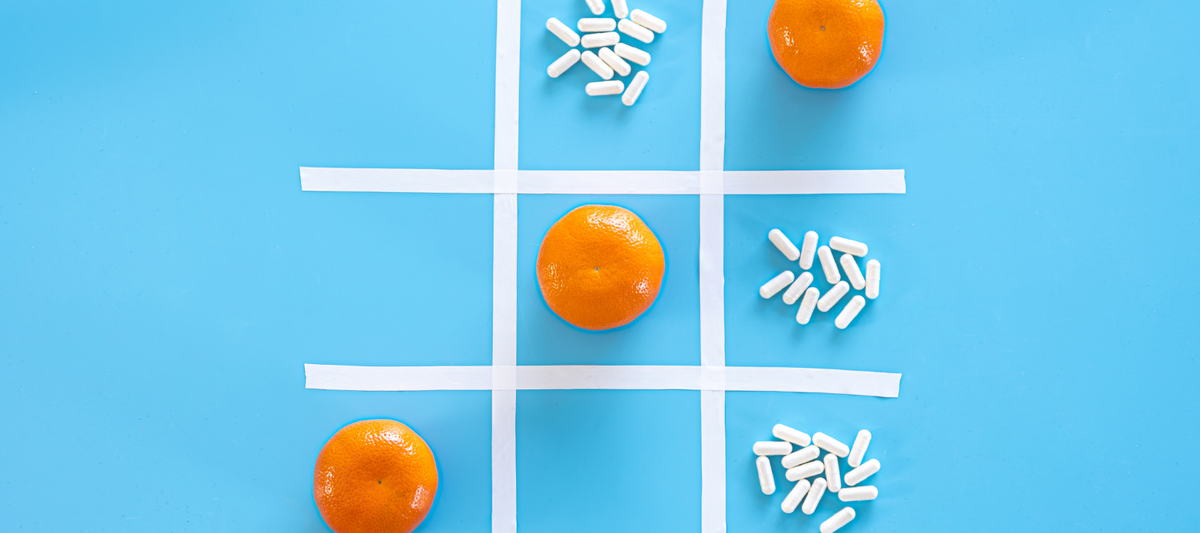 Tic-Tac-Toe-Muster aus weißen Kapseln und Orangenspalten auf hellblauem Hintergrund