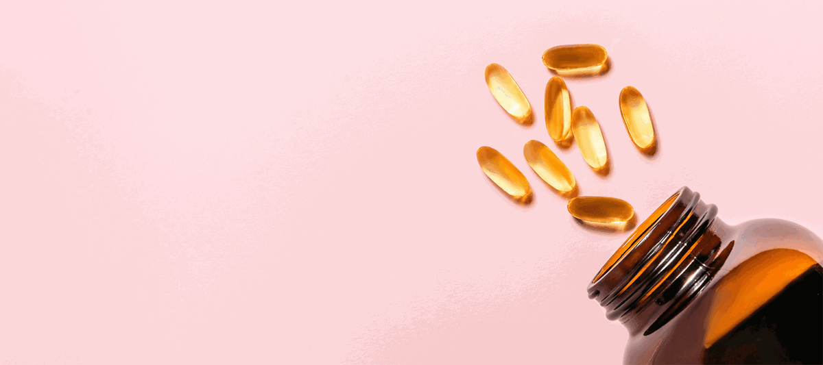 Goldene Omega-3-Kapseln fallen aus brauner Glasflasche auf rosafarbenem Hintergrund
